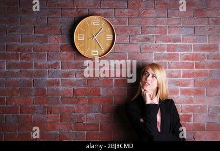 Young attractive woman under the clock, on brick wall background Stock Photo