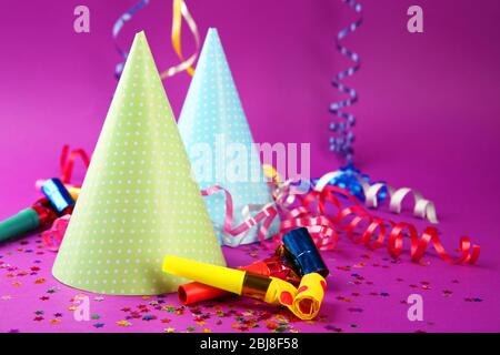 Two Birthday hats with serpentine streamer and noise makers on purple background Stock Photo