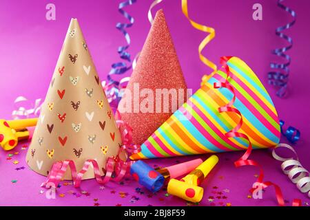 Three Birthday hats with serpentine streamer and noise makers on purple background Stock Photo