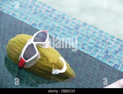 Green coconut in diving goggles floating in the pool Stock Photo