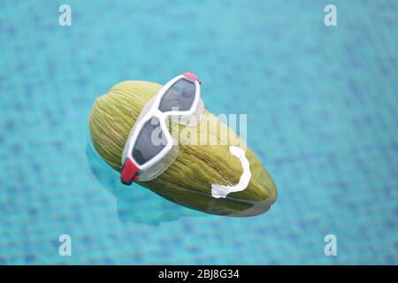 Green coconut in diving goggles floating in the pool Stock Photo