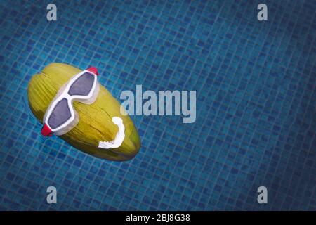 Green coconut in diving goggles floating in the pool Stock Photo