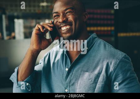 Businessman talking on phone standing in office. Smiling young african man speaking on mobile phone at work. Stock Photo