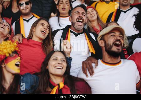 Group of man and woman enjoying watching a match. German football team supporters cheering for their national team during watching a match from stadiu Stock Photo