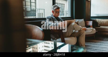 Mature businessman sitting in office lobby with a laptop. Male executive working in office lounge. Stock Photo