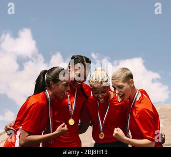 Excited female soccer players shouting in joy after winning the championship. Woman football team with medals celebrating victory. Stock Photo