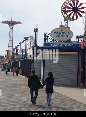 New York, USA. 19th Apr, 2020. Few passers-by walk along the beach boulevard of Coney Island. (to dpa 'New York City Mosaic: Of Ghost Houses and Trust in God') Credit: Benno Schwinghammer/dpa/Alamy Live News Stock Photo
