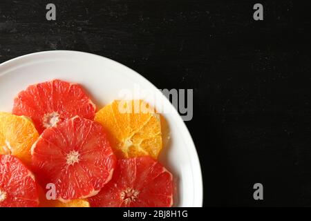 Plate of fresh peeled and sliced citrus on dark wooden background Stock Photo