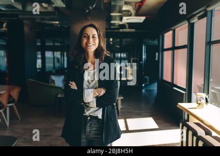 Confident businesswoman standing in office. Smiling woman standing with her arms crossed looking at camera. Stock Photo