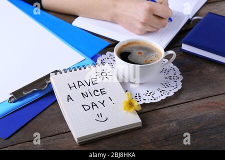 Female hands writing in notebook near cup of coffee and note HAVE A NICE DAY on wooden table closeup Stock Photo