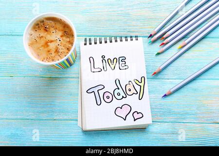 Cup of coffee with note LIVE TODAY and crayons on wooden background Stock Photo