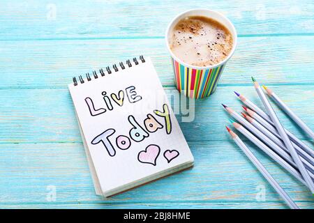 Cup of coffee with note LIVE TODAY and crayons on wooden background Stock Photo