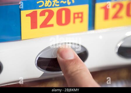 A finger pressing a button on a Japanese vending machine to buy a drink beverage. Translation: cold (drink) Stock Photo