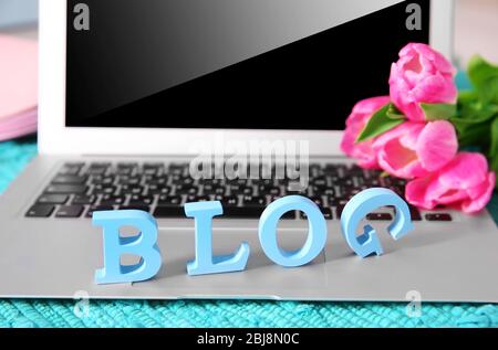Laptop with word BLOG and fresh tulips on blue mat closeup Stock Photo