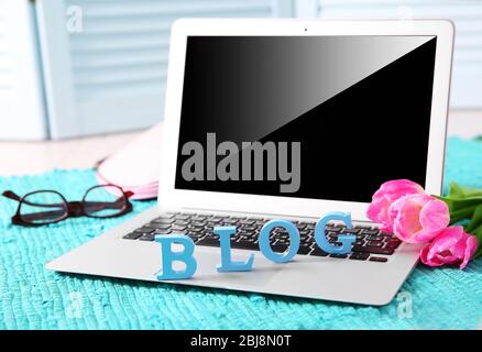 Laptop with word BLOG and fresh tulips on blue mat closeup Stock Photo