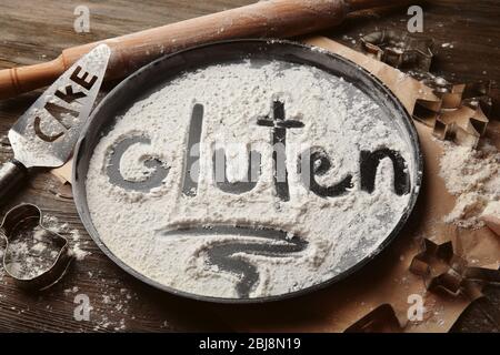 Gluten word written with flour on baking utensil over wooden table Stock Photo