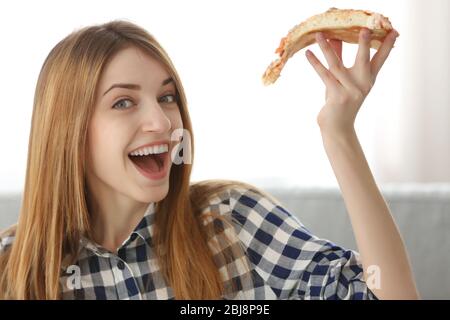 Happy young woman holding slice of hot pizza at home Stock Photo