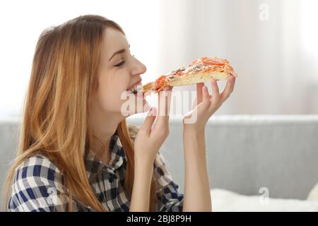 Happy young woman eating slice of hot pizza at home Stock Photo