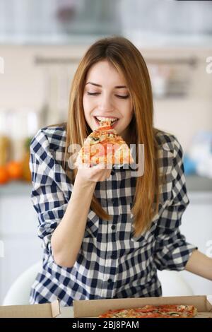 Happy young woman eating slice of hot pizza at home Stock Photo
