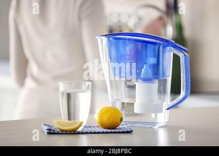 Water filter jug with lemon and glass on kitchen table Stock Photo