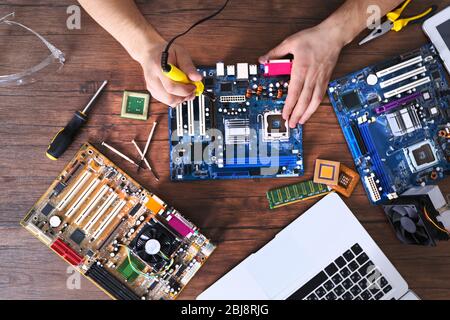Male hands soldering motherboard on wooden table, top view Stock Photo