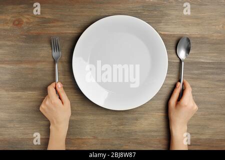 Female hands with cutlery and empty plate on wooden background Stock Photo