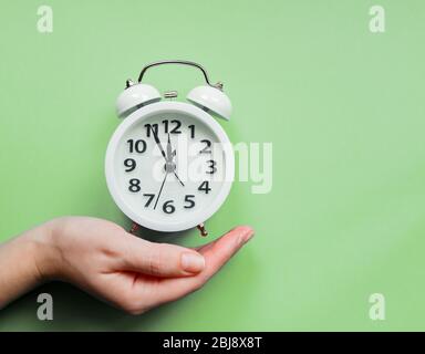 female hand holding an alarm clock on pastel green background Stock Photo