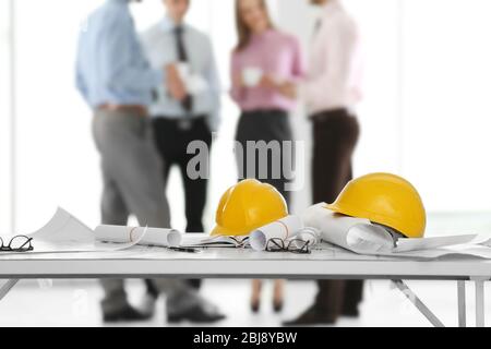 Helmets with blueprints on table and engineers on background Stock Photo
