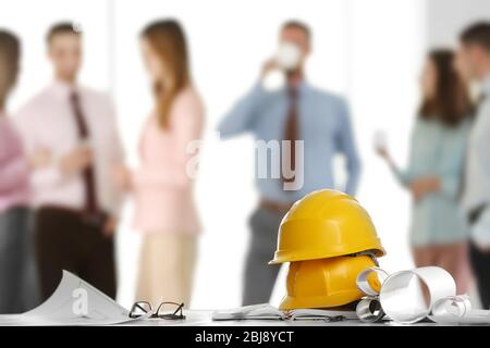 Helmets with blueprints on table and engineers on background Stock Photo
