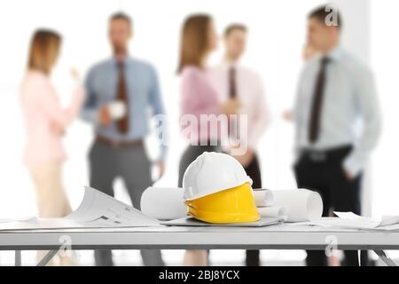 Helmets with blueprints on table and engineers on background Stock Photo