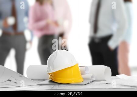 Helmets with blueprints on table and engineers on background Stock Photo