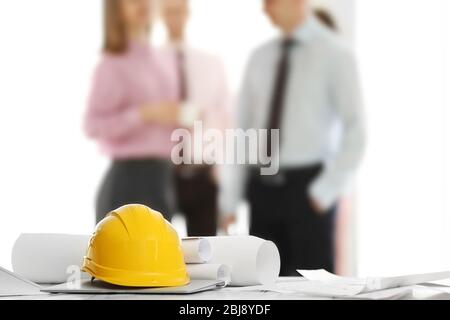Helmets with blueprints on table and engineers on background Stock Photo
