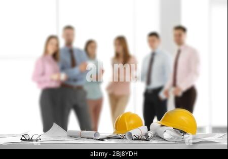 Helmets with blueprints on table and engineers on background Stock Photo