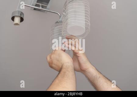 man unscrew glass shades from the chandelier. house cleaning with chandelier washes. husband for an hour Stock Photo