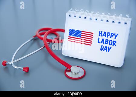 Notebook with printed text HAPPY LABOR DAY and stethoscope on grey background Stock Photo