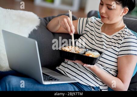 Young Asian woman eating while watching something on a laptop. Stock Photo