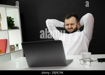 Overworked handsome businessman in white shirt with closed eyes and hands on back of head tired of remote freelance work, burnout, financial problems Stock Photo
