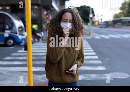 Caucasian woman wearing a protective mask and coughing out in the streets Stock Photo