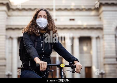 Caucasian woman wearing a protective mask on her bike, wearing earphones in the streets Stock Photo