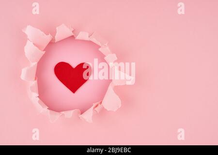 Valentine's Day. A ripped hole and red heart in bright pink textured background, concept of rupted paper with copy space. Long width side banner Stock Photo