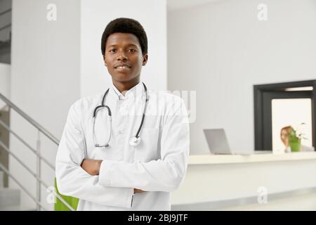 Selective focus of professional therapist with stethoscope on neck posing with arms crossed and looking at camera. Portrait of smiling african male do Stock Photo