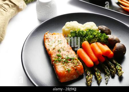 Tasty dish with baby carrots and salmon on black plate closeup Stock Photo