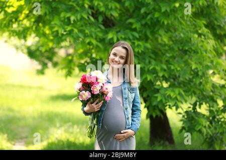 Pregnant woman with peony bouquet in park Stock Photo