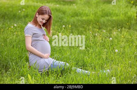 Beautiful pregnant woman sitting on grass Stock Photo