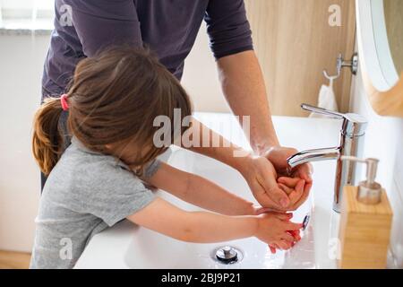 Caucasian father teaching little child girl how to wash hands in bathroom during covid-19 pandemic lockdown. Dad and baby daughter washing hands at si Stock Photo
