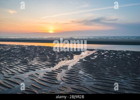 Beautiful pattern of waves and ripples in the wet sand of the beach after the sea recedes (low tide). Colorful sunset over sea. Stock Photo