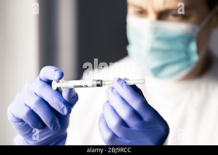 Doctor or nurse looking at a syringe needle for coronavirus vaccine. Medical professional or scientist working in lab for research. Stock Photo