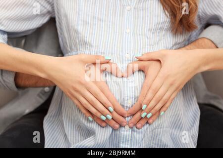 Pregnant woman and husband holding hands in heart shape on her baby bump Stock Photo