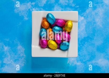 solid milk chocolate mini Easter eggs foil wrapped in bowl on blue patterned background - looking down on from above Stock Photo