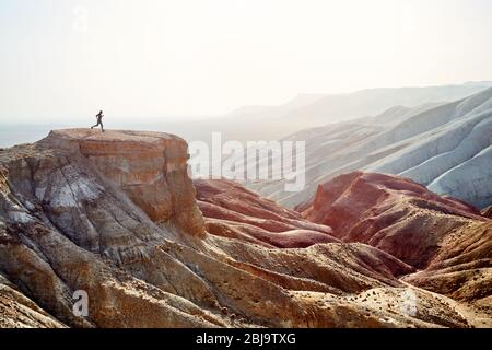 Silhouette of runner athlete on the big rock in canyon with red desert mountains